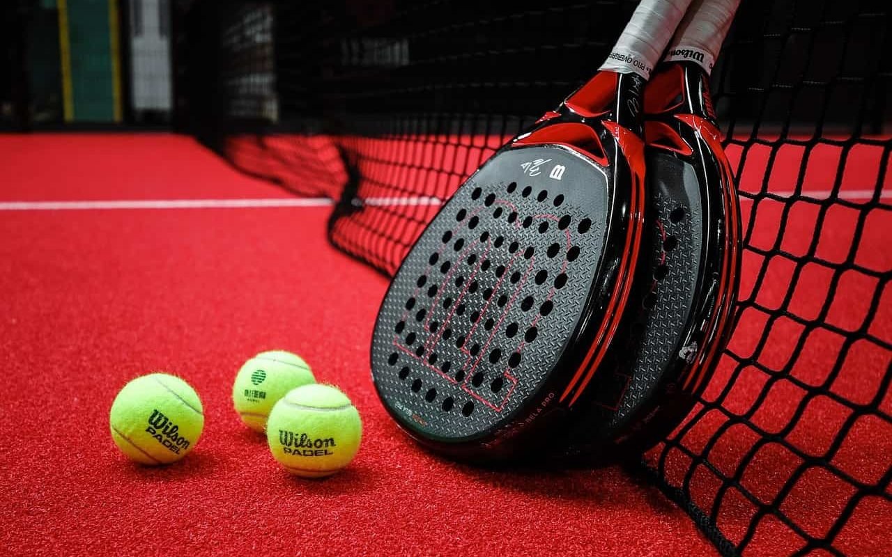 Équipement de padel professionnel avec raquettes et balles Wilson sur un court rouge, essentiel pour tout business plan pour padel.