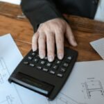 Main sur calculatrice, plans et feuilles sur table en bois