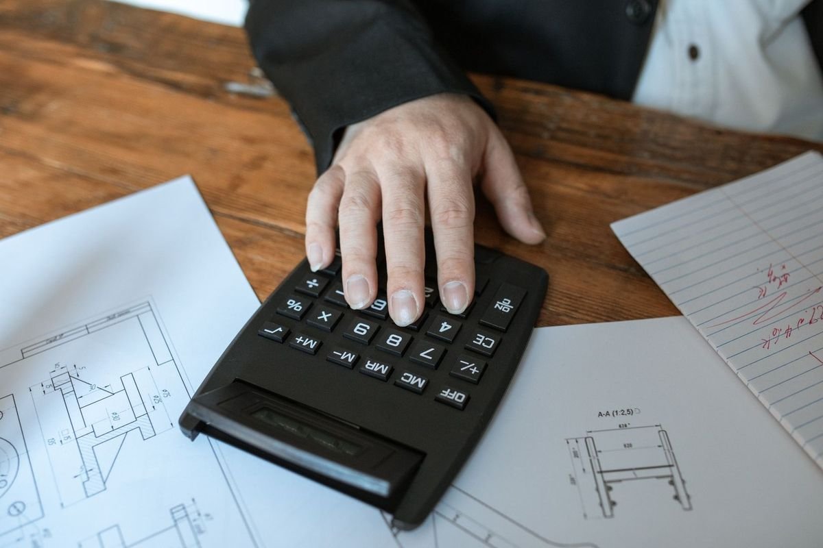 Main sur calculatrice, plans et feuilles sur table en bois