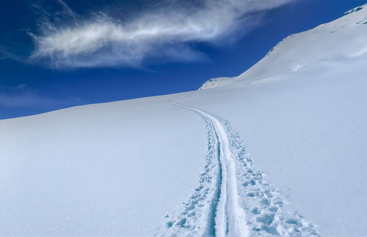 Piste de ski en poudre sur une montagne enneigée sous un ciel bleu avec nuages