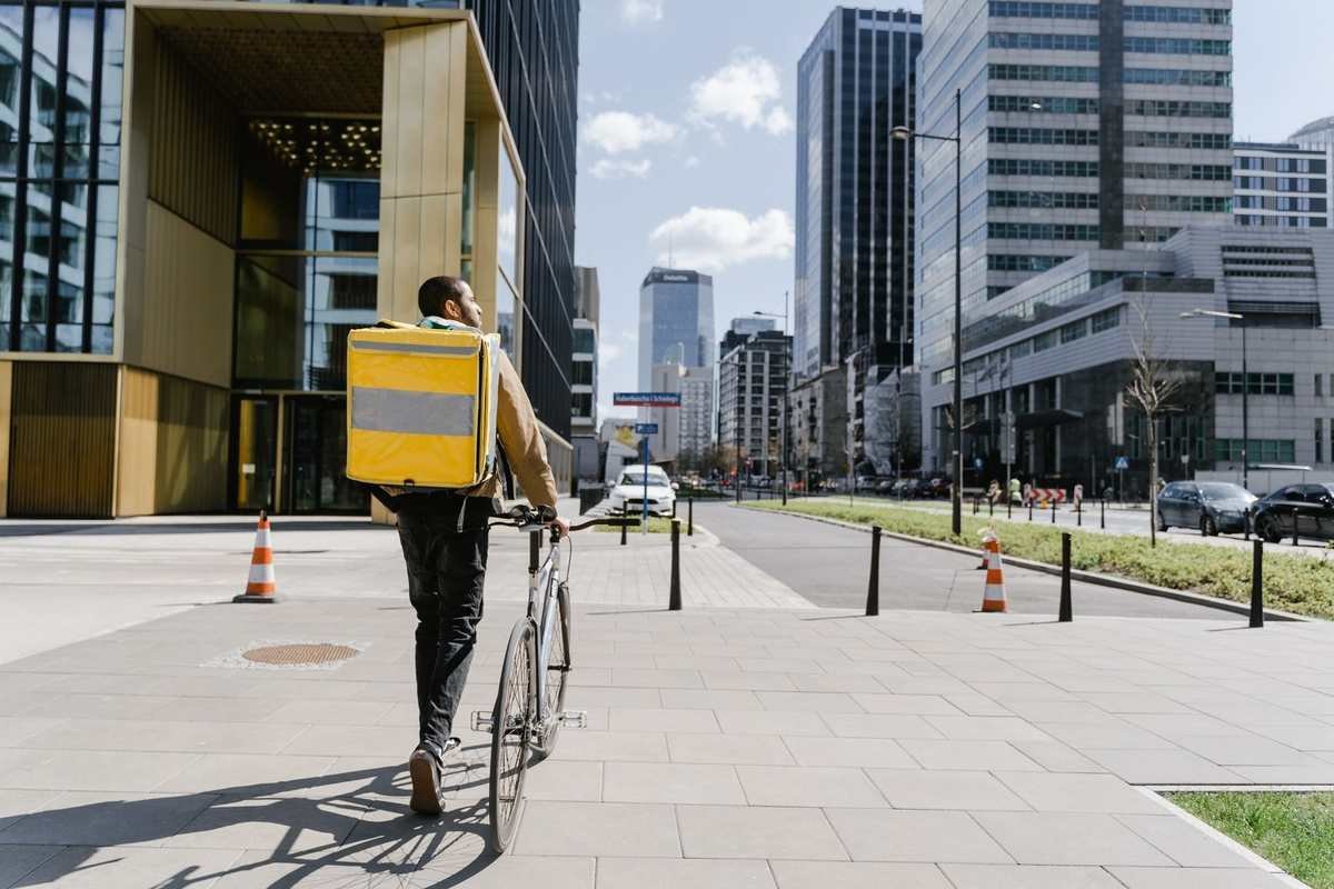 Homme à vélo portant un sac jaune sur un trottoir urbain Homme à vélo portant un sac jaune sur un trottoir urbain
