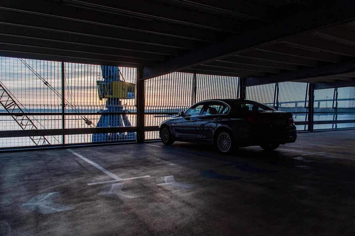 Voiture dans un parking souterrain, devant une fenêtre donnant sur un grue et un ciel coloré Voiture dans un parking souterrain, devant une fenêtre donnant sur un grue et un ciel coloré