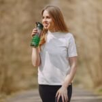 Une femme boit depuis une gourde verte sur un sentier